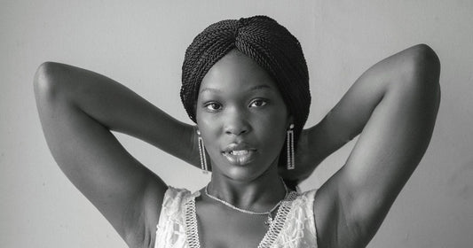 Black and white portrait of a woman with long twisted braids wrapped into a crown-style updo, hands behind her head