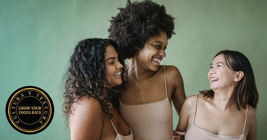 Three smiling women against a green wall, one with a full curly afro, one with long dark spiral curls and one with straight shoulder-length hair