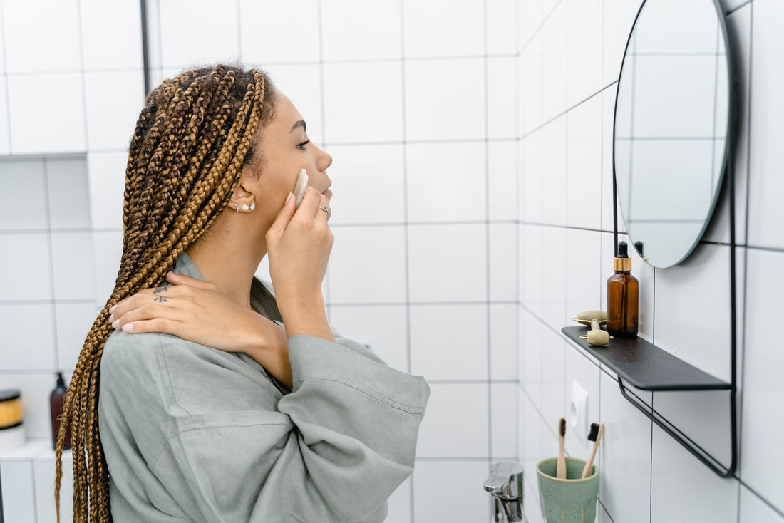 Black woman with long honey blonde braids looking into a bathroom mirror during her self care routine