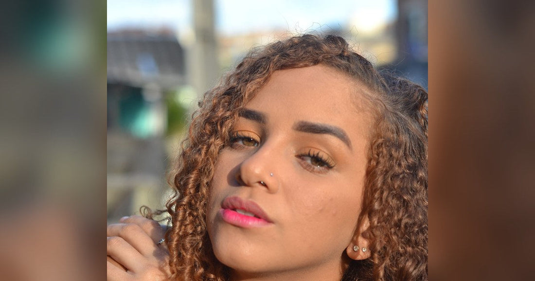 Woman with long, honey brown curly hair in warm afternoon sunlight, resting her hand near her shoulder