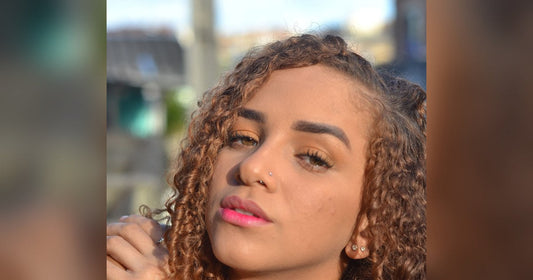 Woman with long, honey brown curly hair in warm afternoon sunlight, resting her hand near her shoulder