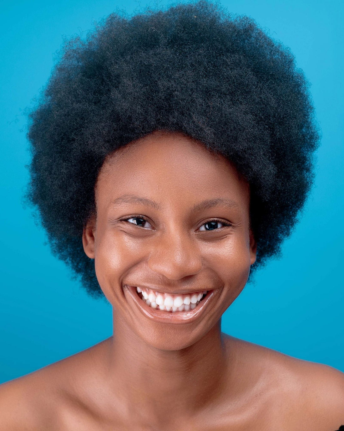 Black woman with a full natural afro smiling against a blue background
