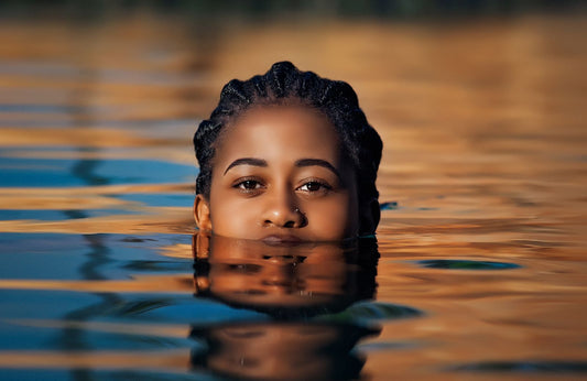 Black woman with braided hair emerging from calm water at sunset