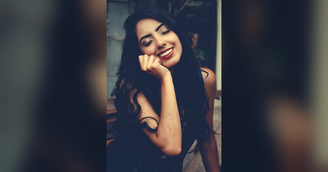 Smiling woman with long dark wavy hair resting her chin on her hand