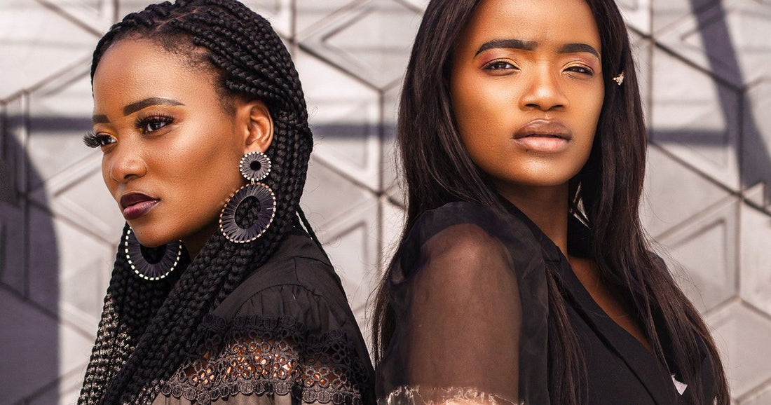 Two Black women back to back, one wearing long box braids and one wearing long sleek straight hair, against a geometric wall