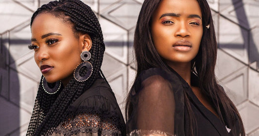 Two Black women back to back, one wearing long box braids and one wearing long sleek straight hair, against a geometric wall