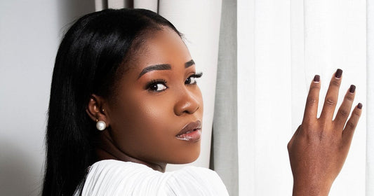 Black woman with long, sleek straight hair and a smooth hairline looking over her shoulder by a white curtain