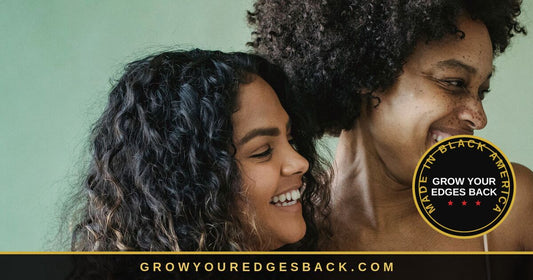Two women laughing together against a soft green backdrop. The woman in front has long dark curly hair falling past her shoulders, with her hairline and the fine baby hairs at her temple clearly visible.