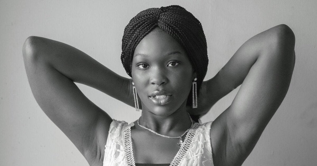Black woman with long twists wrapped up and away from her hairline, hands behind her head, in a black and white portrait