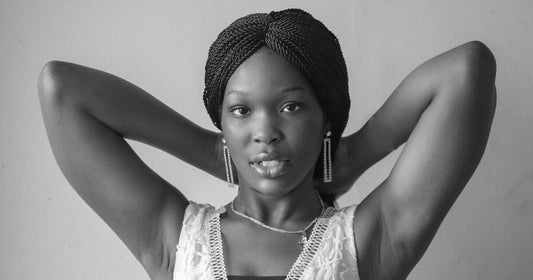 Black woman with long twists wrapped up and away from her hairline, hands behind her head, in a black and white portrait